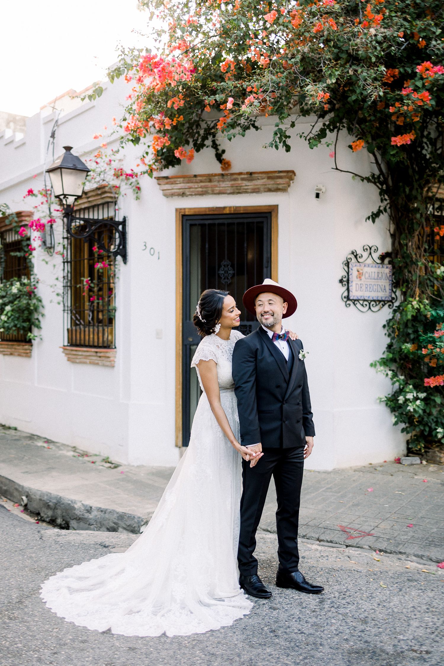 Wedding couple laughing together against a white wall adorned with coral flowering vines.
