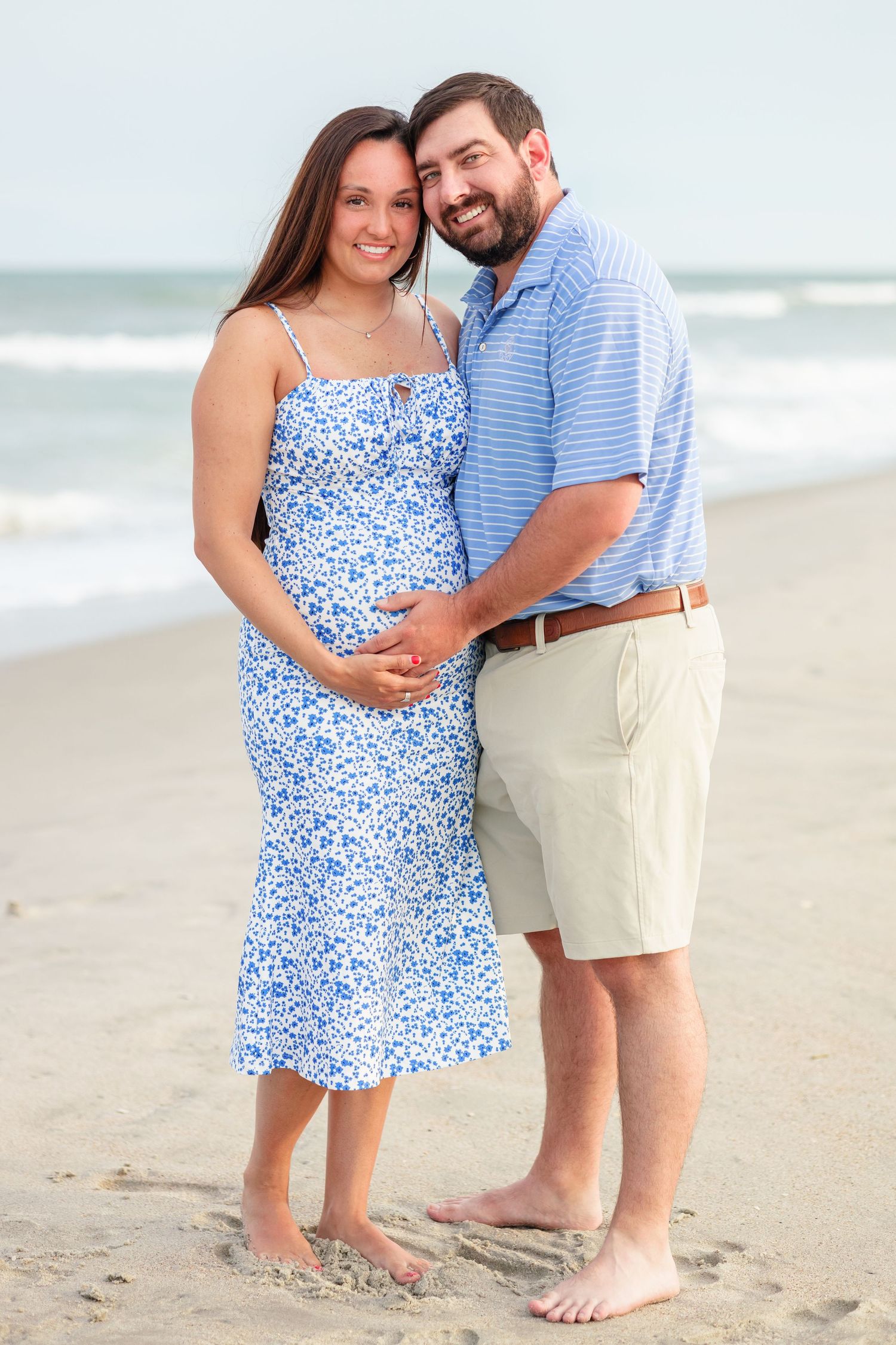 Maternity beach portrait of couple in coordinating blue and khaki outfits.