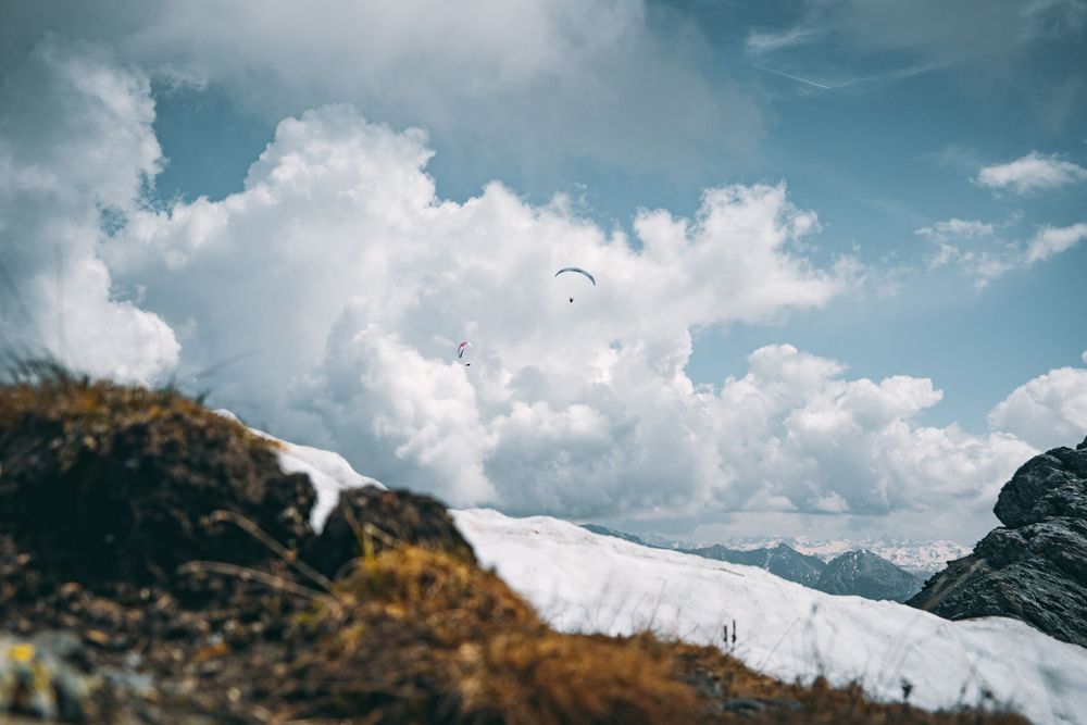 Paraglider soaring over snow-covered mountains against a cloudy sky. Photographer: Urban Engel Perspectiva