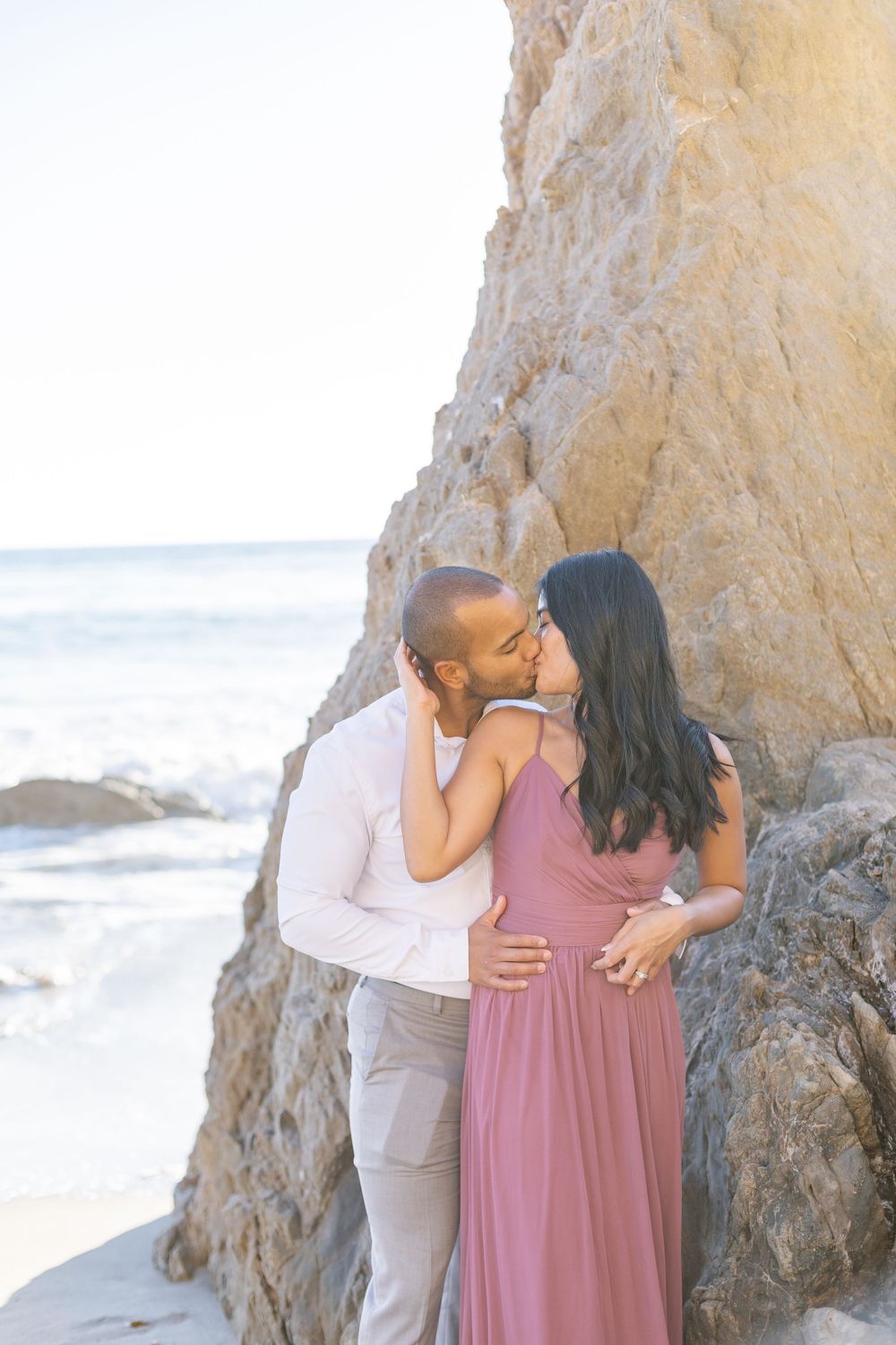A romantic beachside moment captured between a couple near towering coastal cliffs.