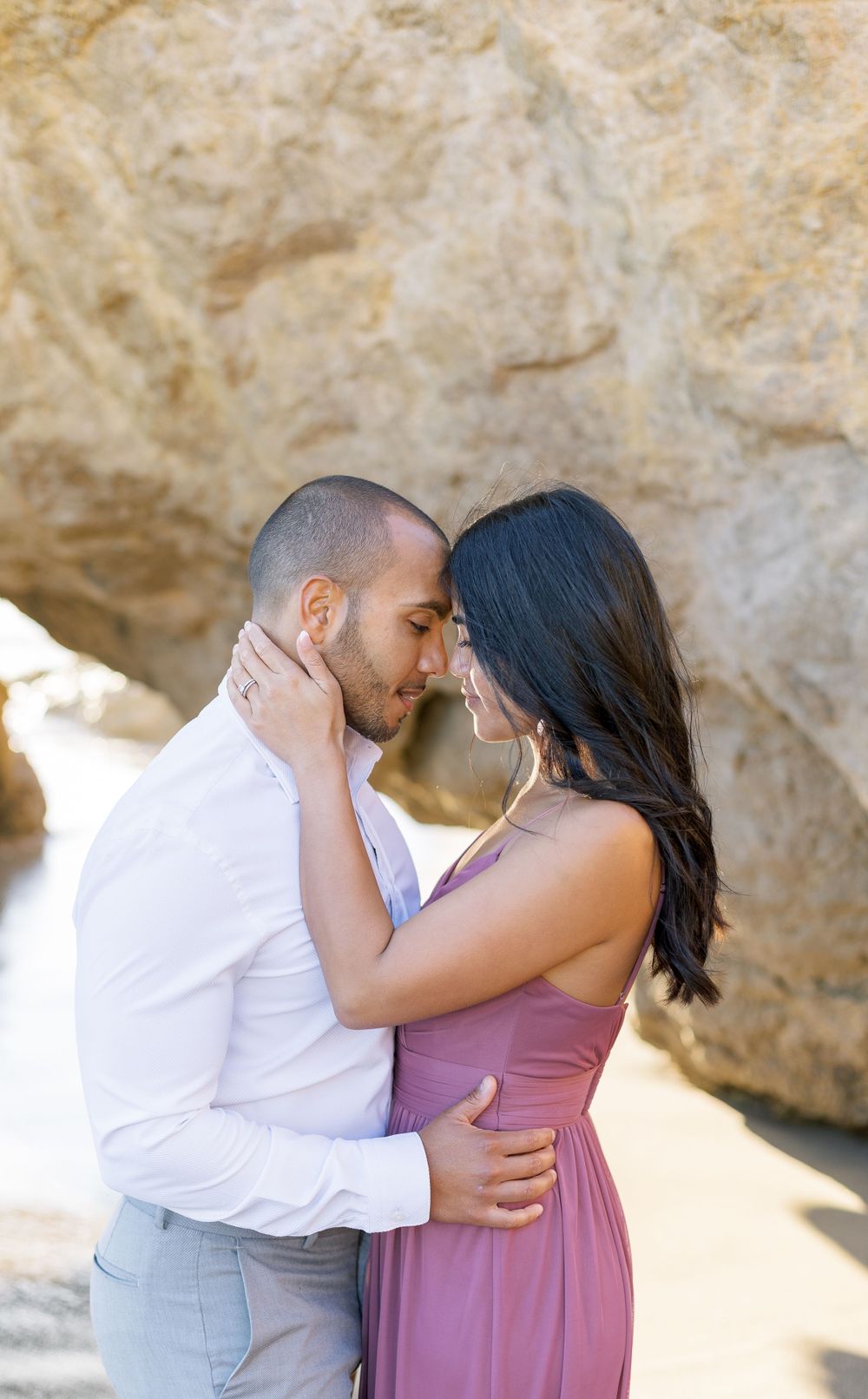 A tender embrace between a couple against a backdrop of beige coastal rocks.