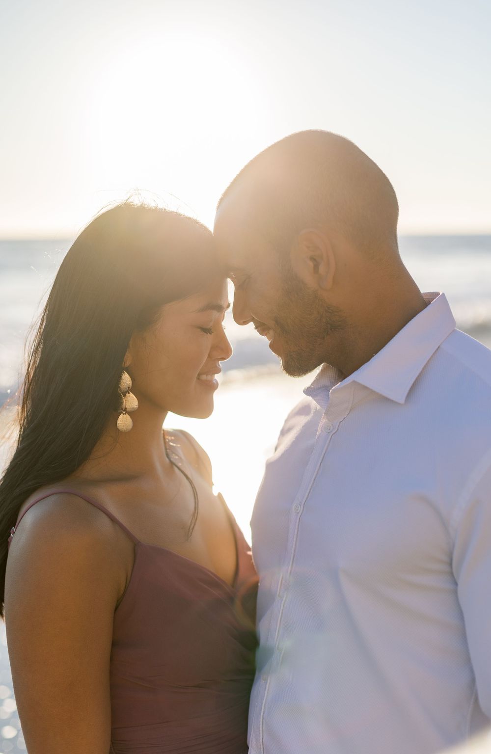 Intimate close-up portrait of couple touching foreheads in golden sunset light at beach.
