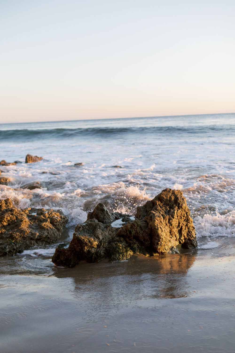 Rocky formations in the ocean surf during sunset with waves crashing on a beach.