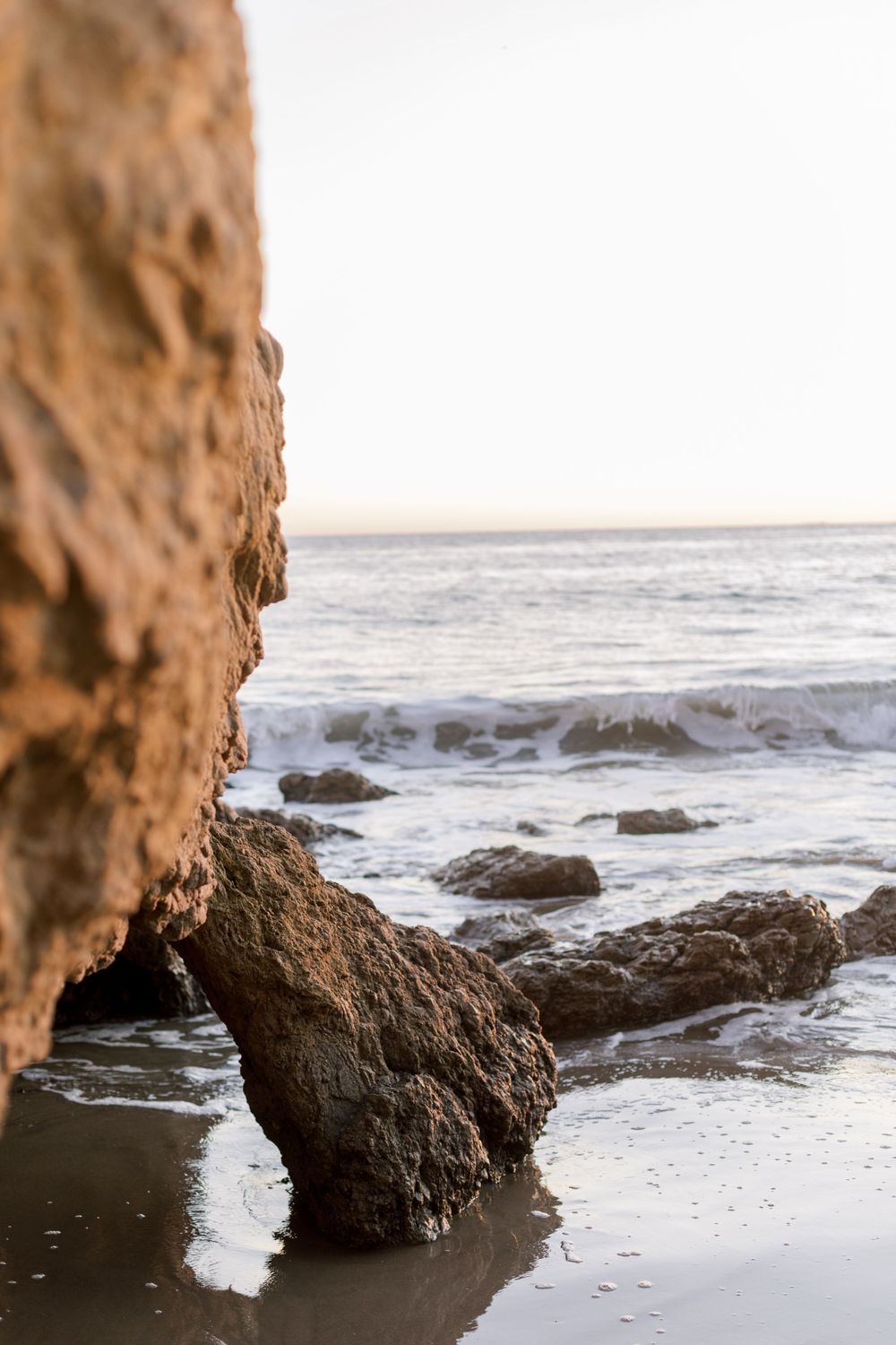 Dramatic coastal rock formations with crashing waves against the shore during golden hour.