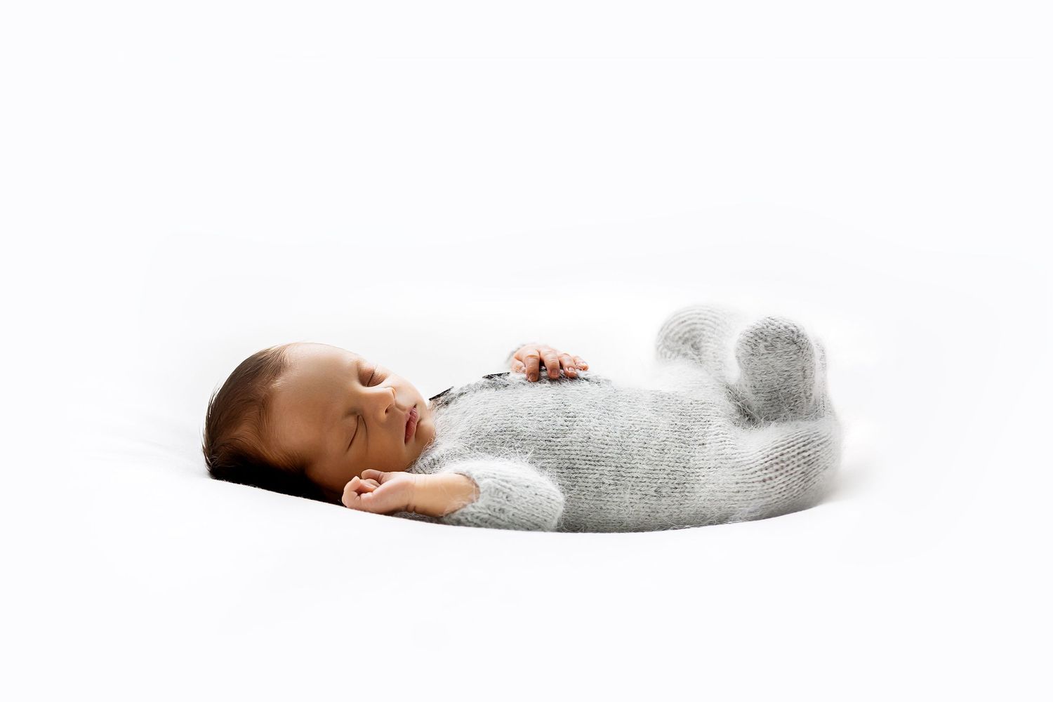 Newborn baby peacefully sleeping in white swaddle on light background.