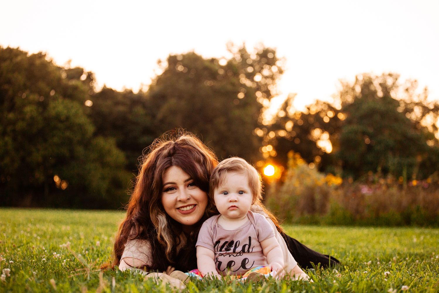 A mother and baby lying on green grass during a golden sunset in a park.