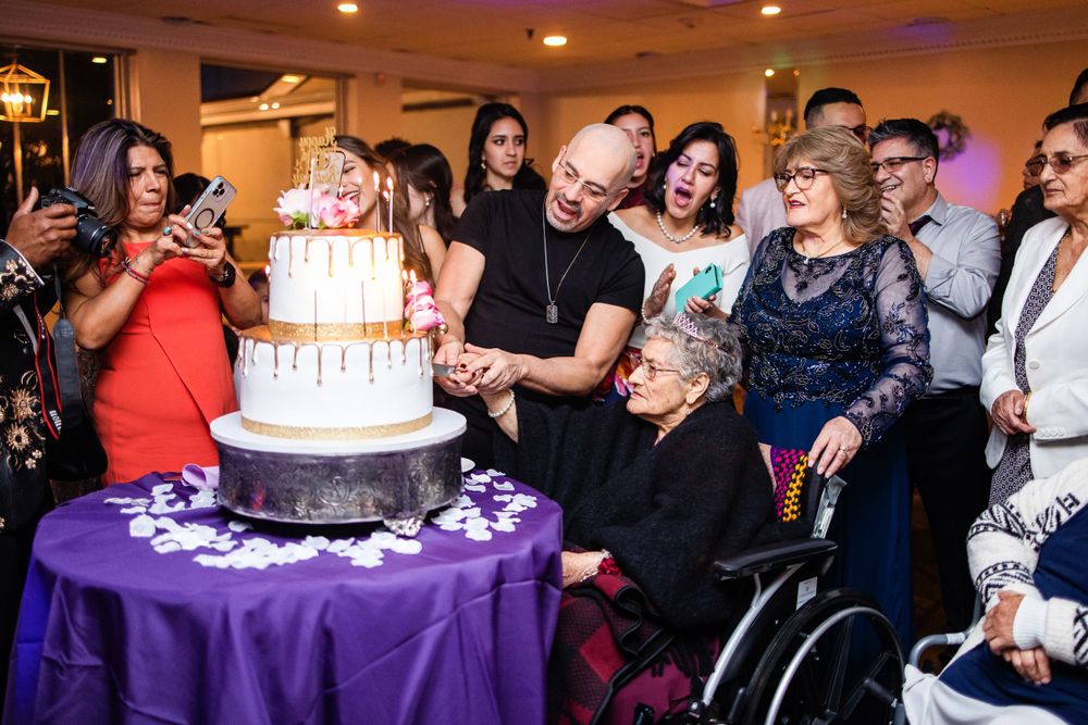 Birthday celebration with guests gathered around a tiered cake on purple table.