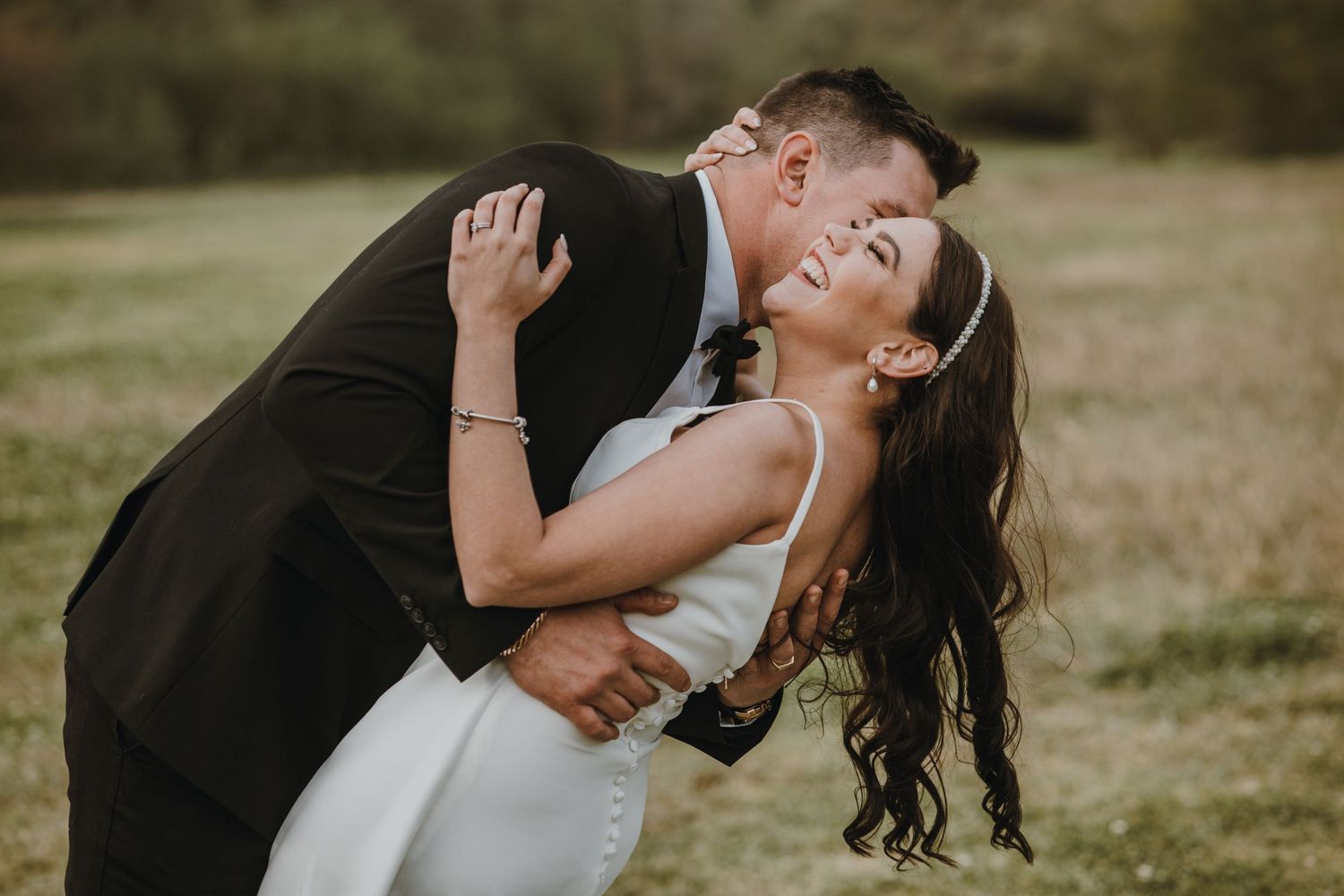 Romantic dip pose of couple in formal attire on grassy hill.