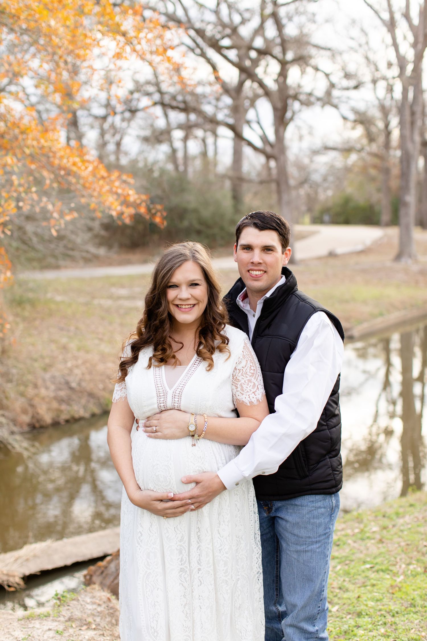 Expecting couple poses by pond during autumn maternity photoshoot.