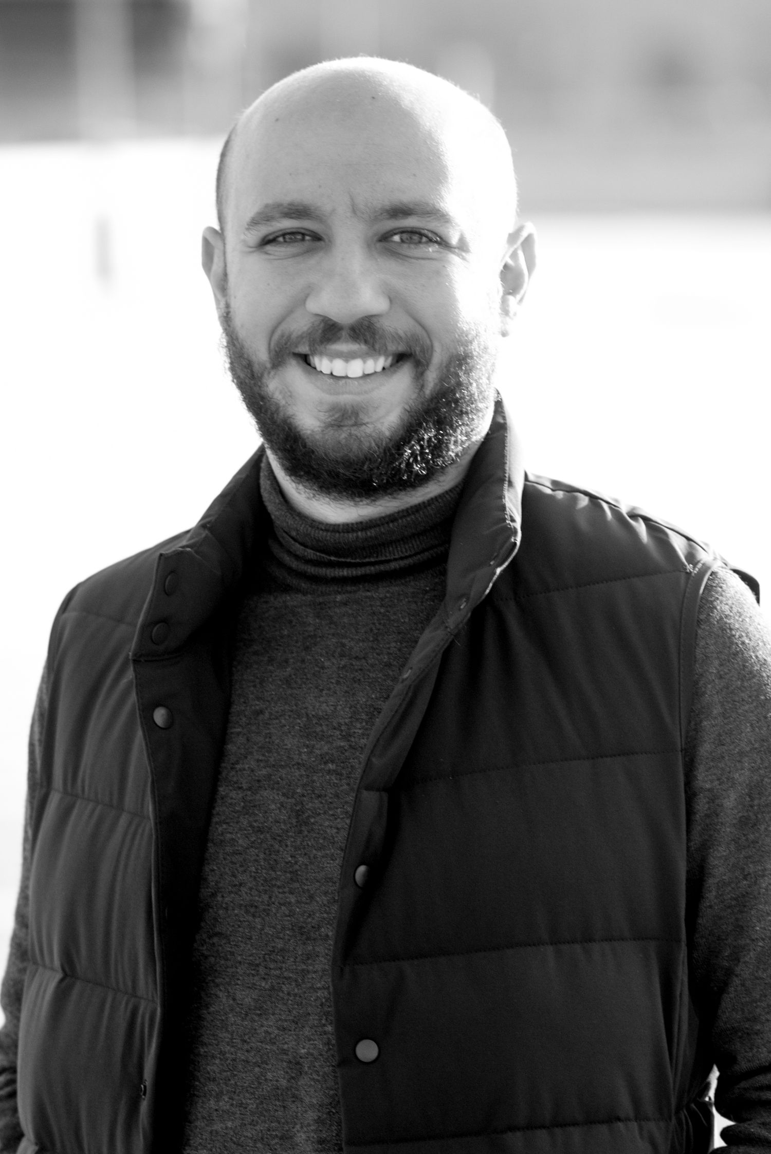 Professional headshot of a Peter Loza wearing a black puffer vest and turtleneck sweater.
