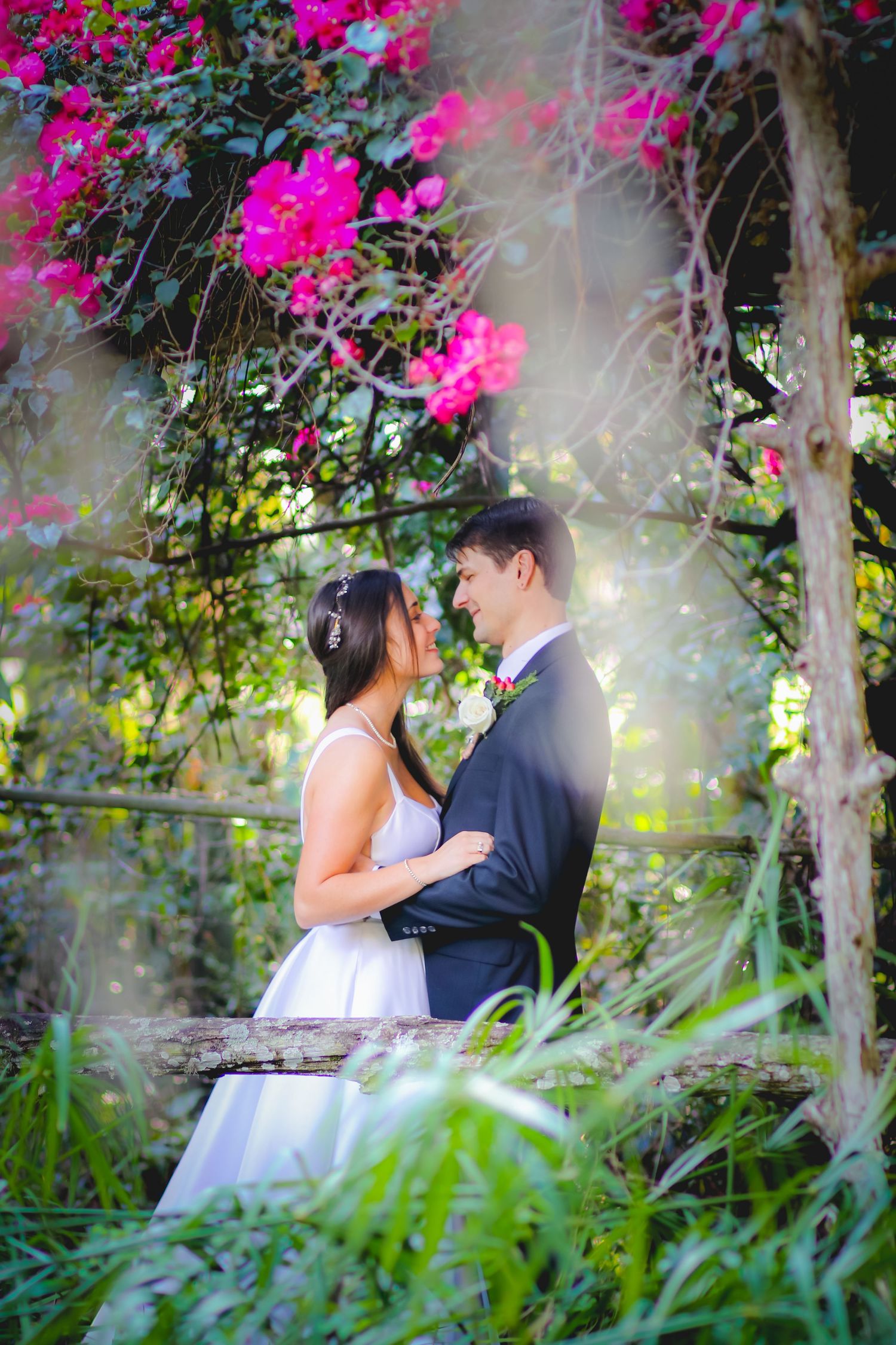 Bride and groom share a romantic moment under a floral arch with vibrant pink bougainvillea in a lush garden at Adam's Ranch in Fort Pierce