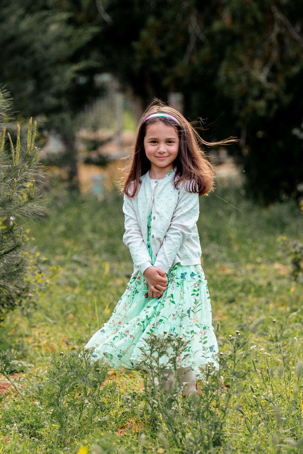 Young girl in mint green outfit twirling in sunny garden setting.