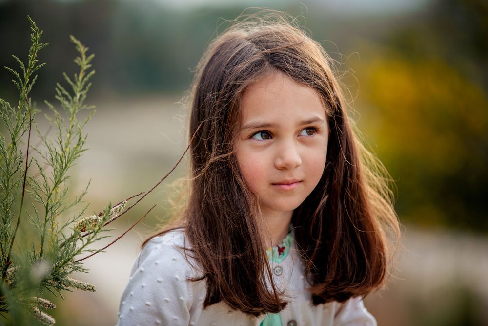 Young child in a mint green dress poses outdoors against a blurred natural background.