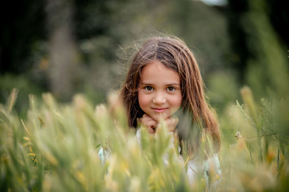 Child playing in tall grass field during golden hour photography session.
