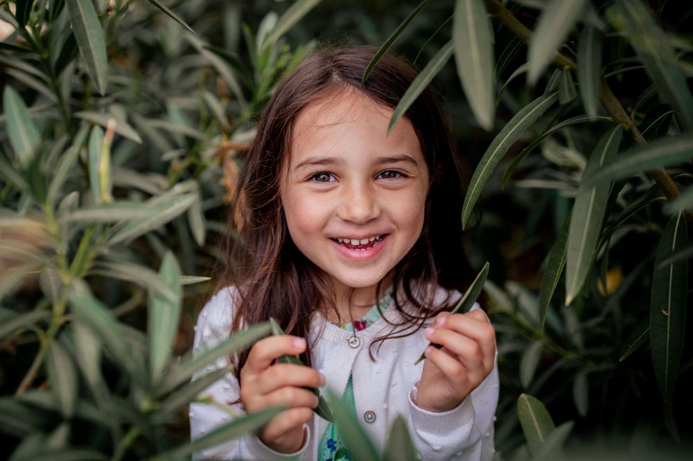 Young child smiling among green foliage in natural outdoor setting.
