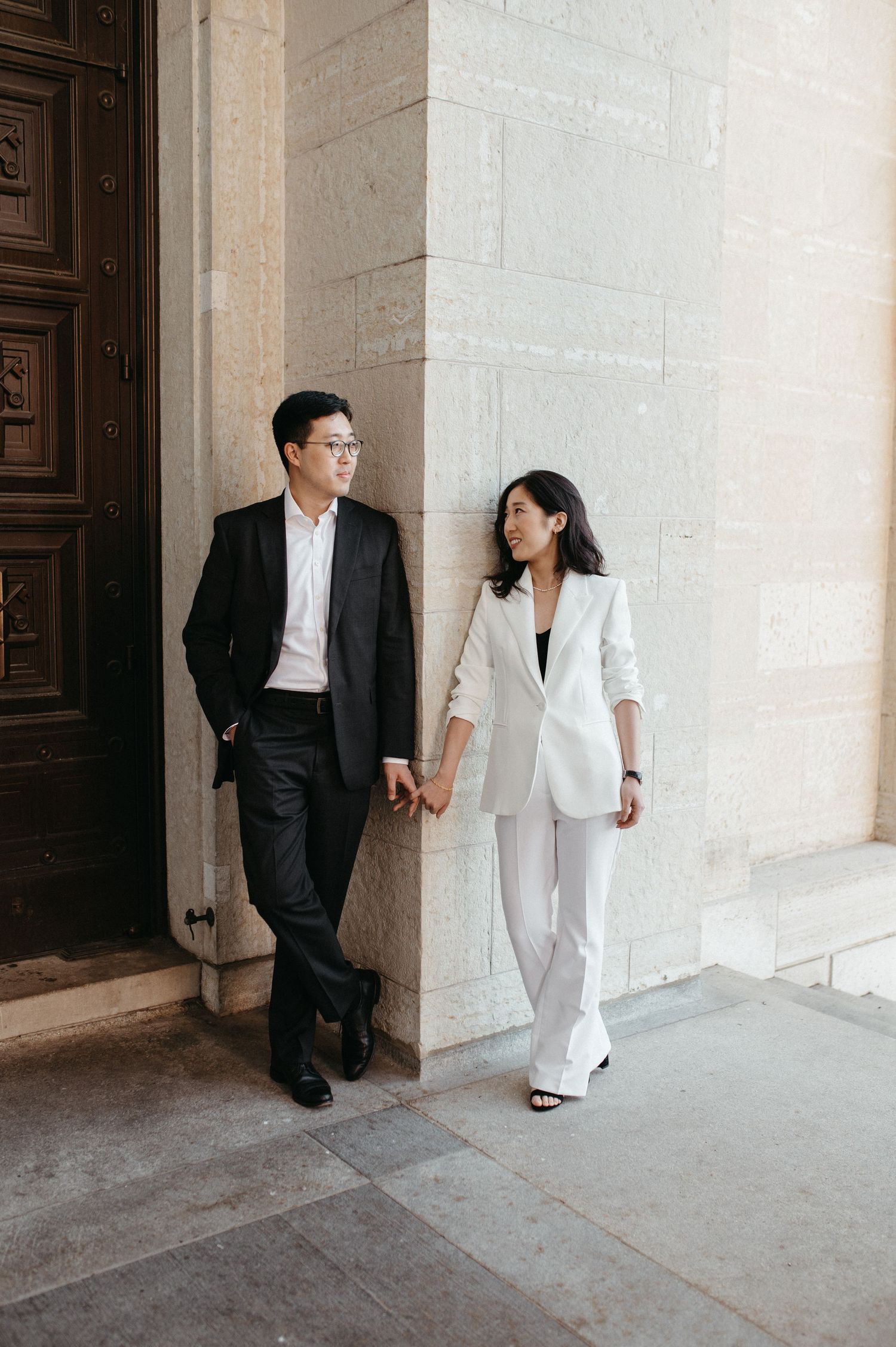 Stylish couple in coordinated black and white outfits holding hands by ornate wooden doors.