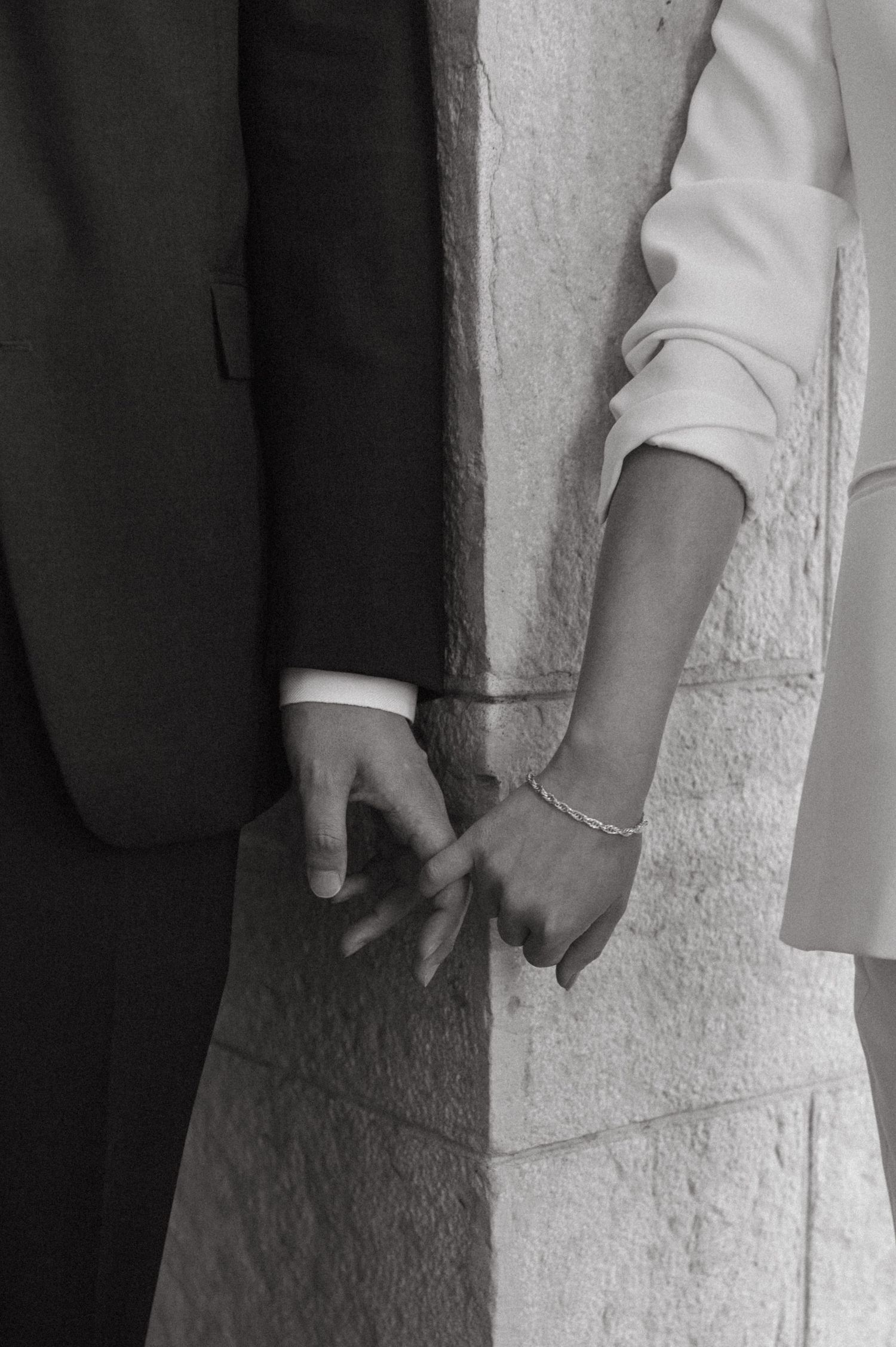Close-up black and white shot of two hands touching against a stone wall.