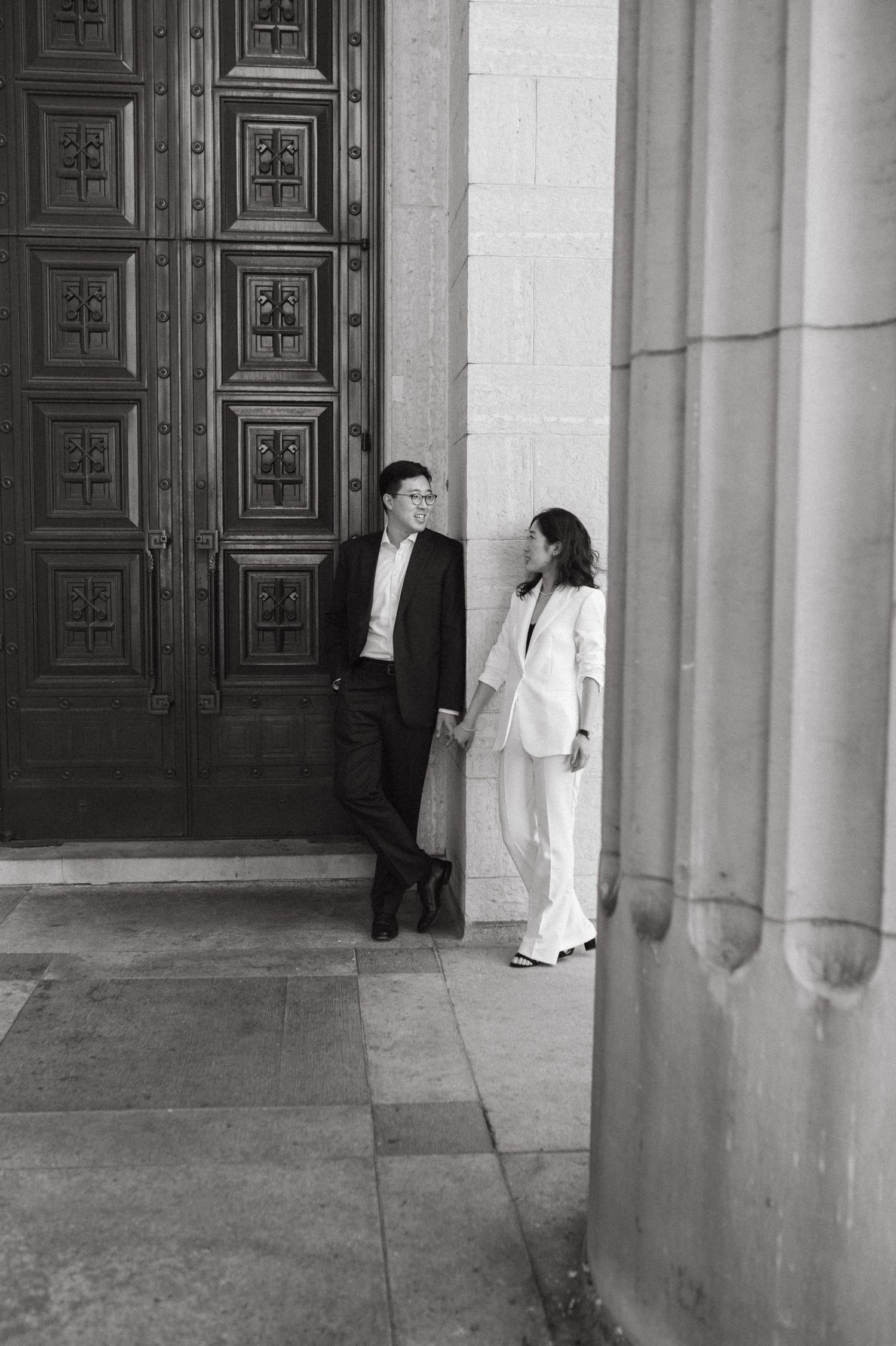 Black and white architectural photo of a couple by decorative wooden doors.