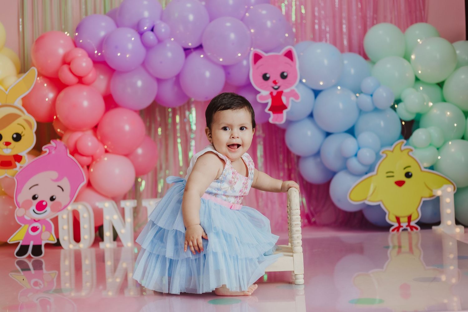 Birthday celebration setup with pastel balloon arch and cartoon characters for young child.