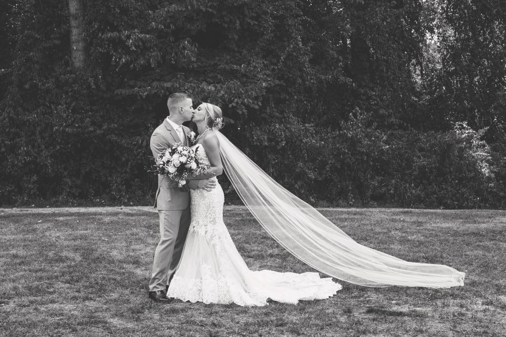 Black and white photo of bride and groom kissing outdoors, brides long veil flowing in the wind.
