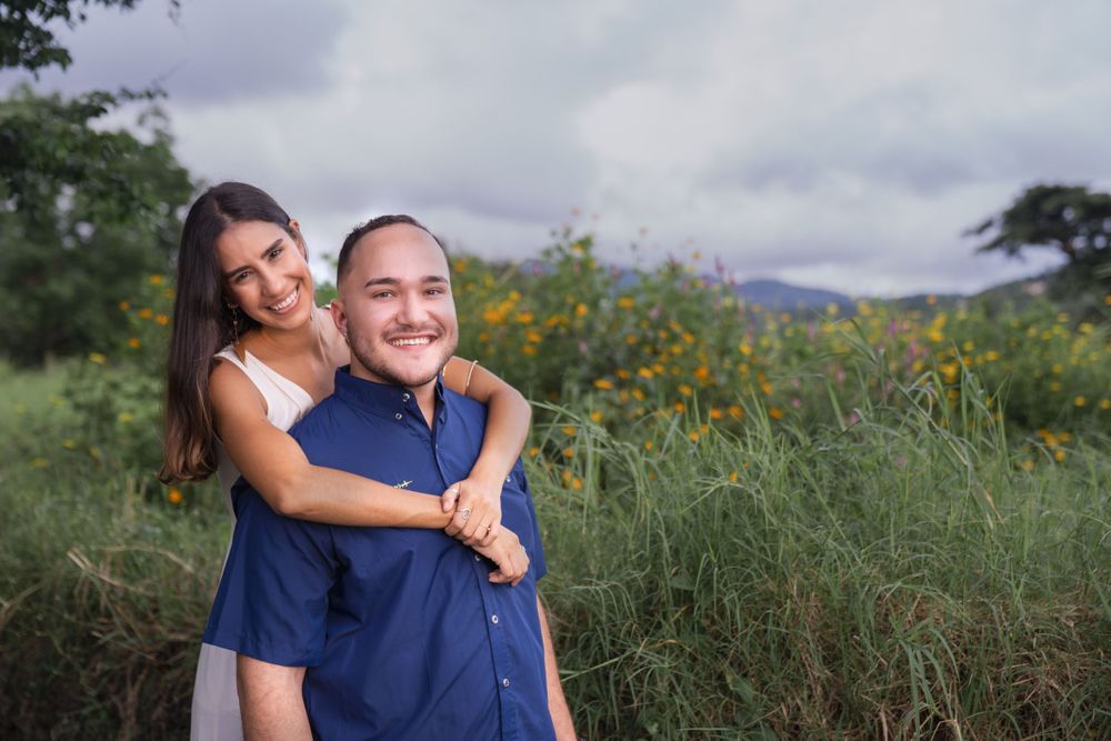 A couple posing together outdoors with yellow wildflowers and mountains in the background.