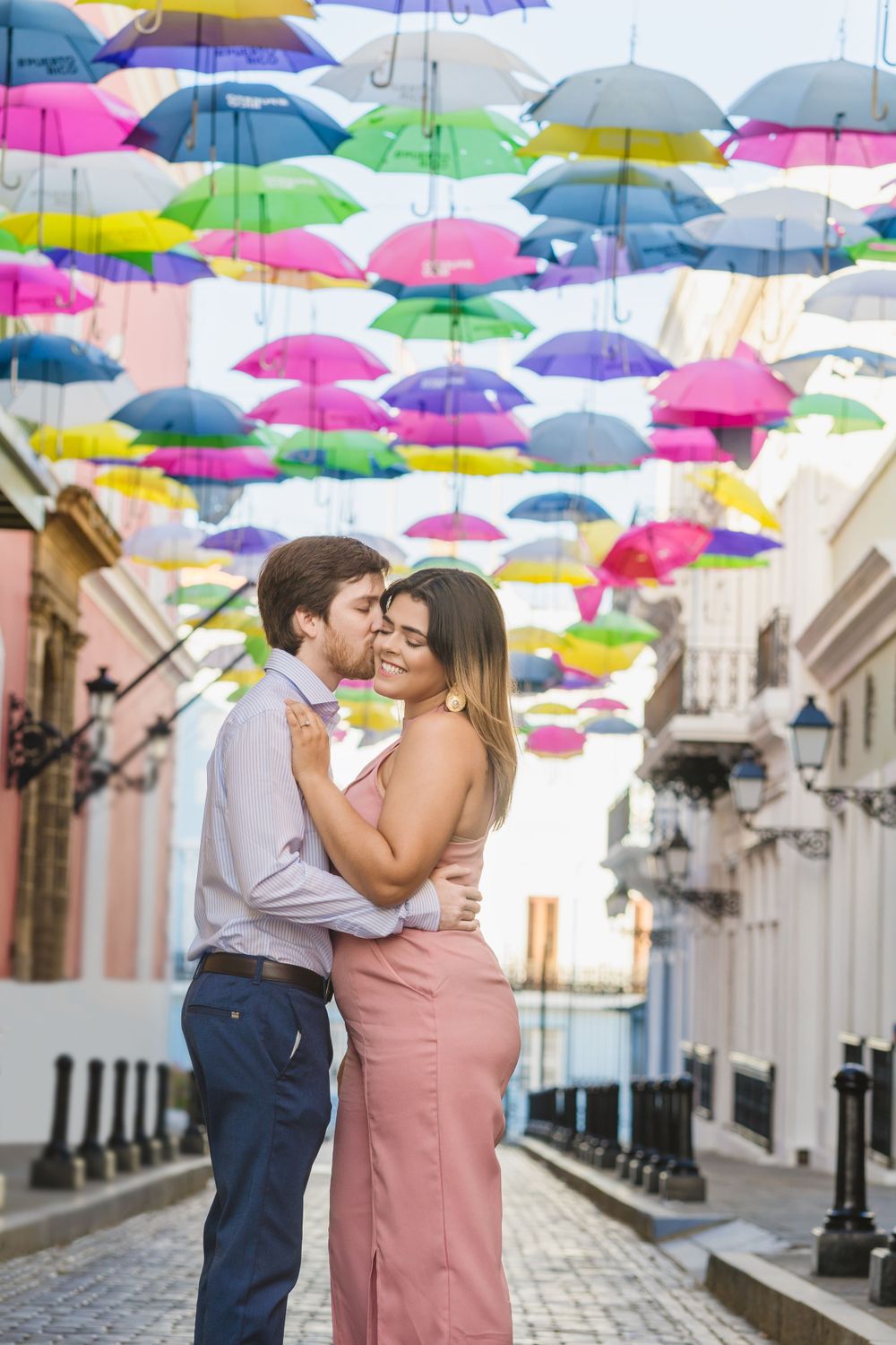A couple embracing under colorful suspended umbrellas in a historic street setting.