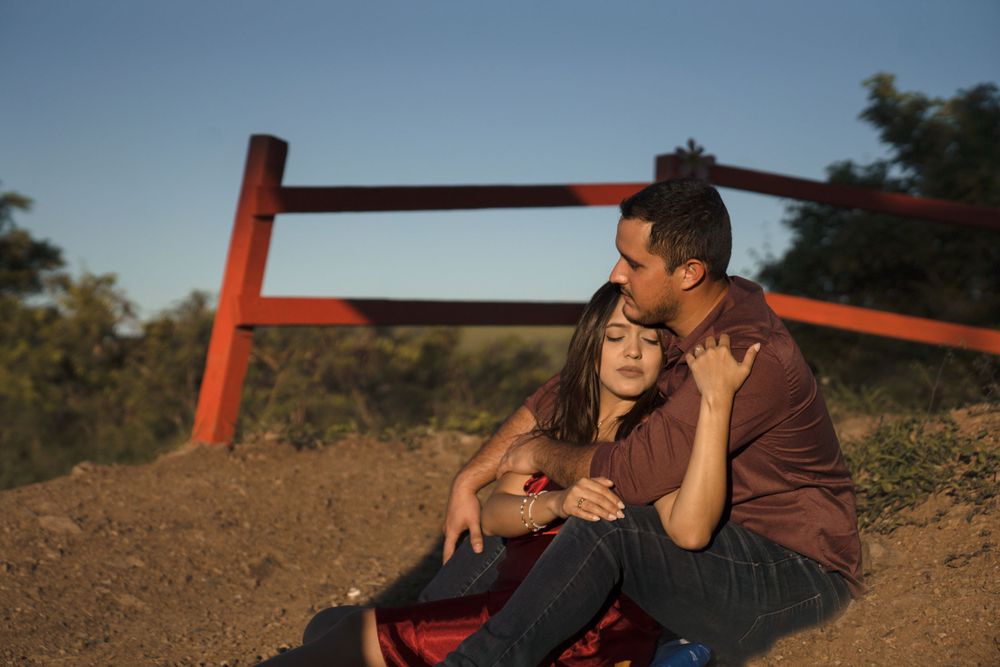 A couple sitting together on a bench against a rustic red fence during golden hour.