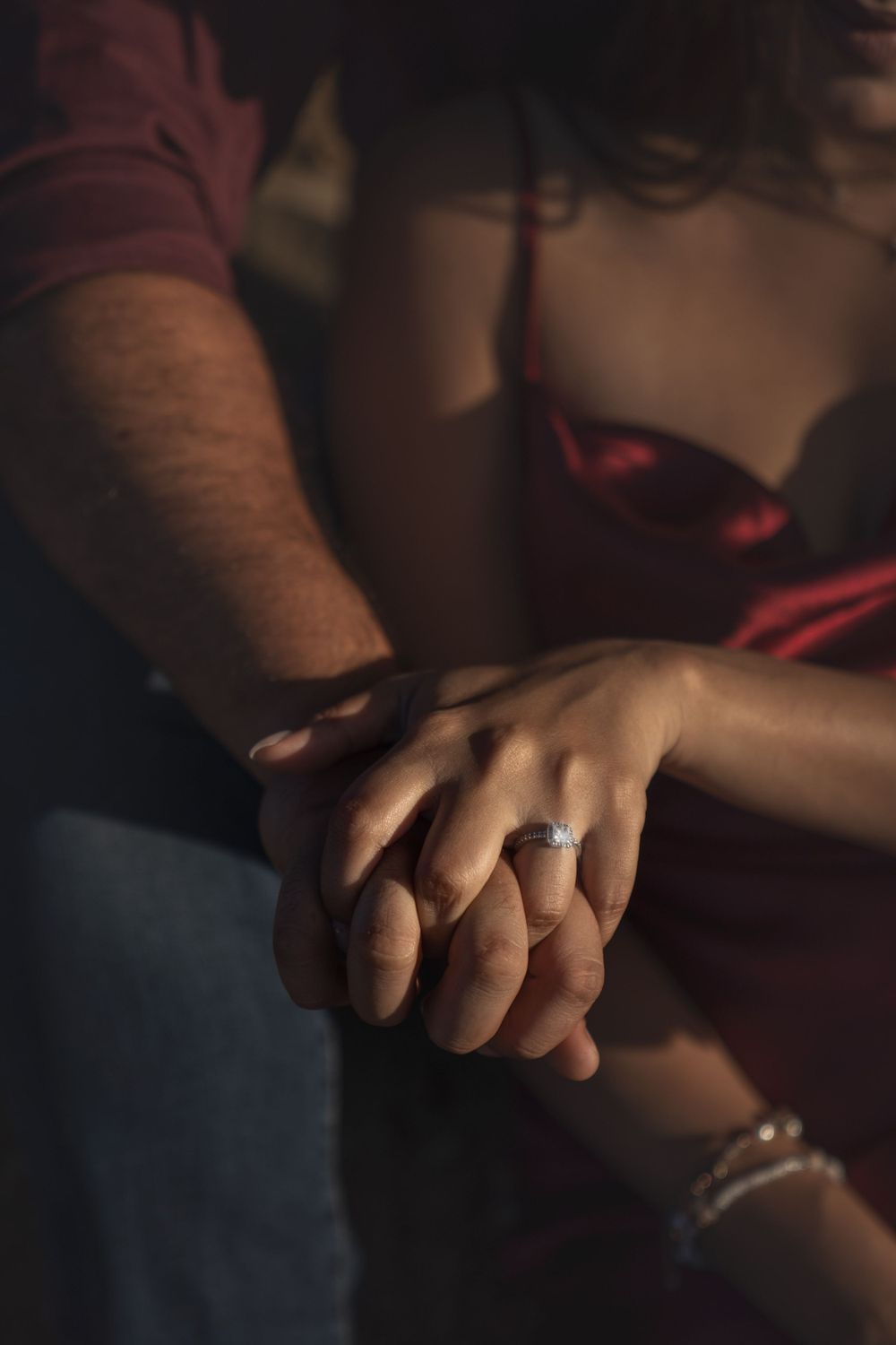 Close-up of two hands clasped together with an engagement ring visible in dim lighting.