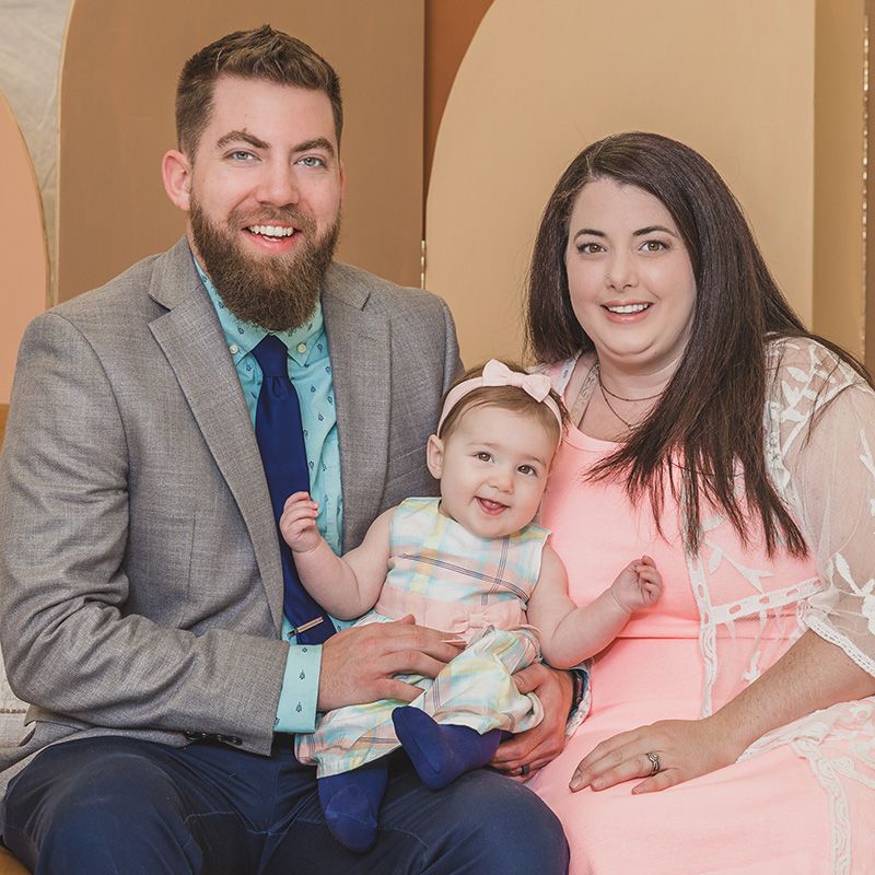 Young couple sitting on a couch smiling with their newborn baby