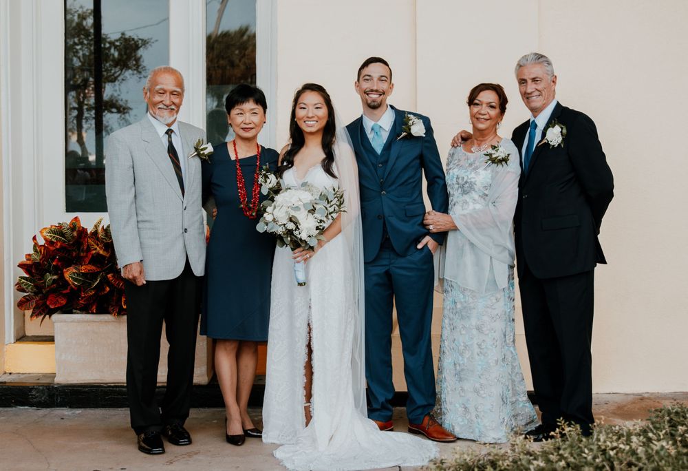 Wedding party group photo outside white building with formal attire.