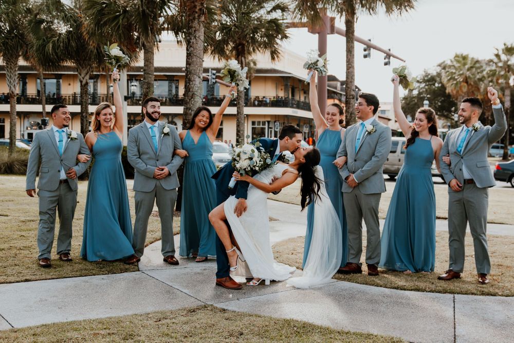 Wedding party in coordinated blue and gray attire posing outdoors.