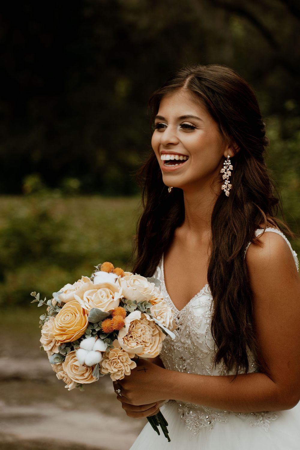 Beautiful bride in lace dress smiling while holding a bouquet of peach and cream roses.