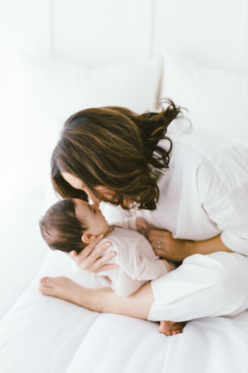 Parent and child sharing affectionate moment on white bedding in natural light.