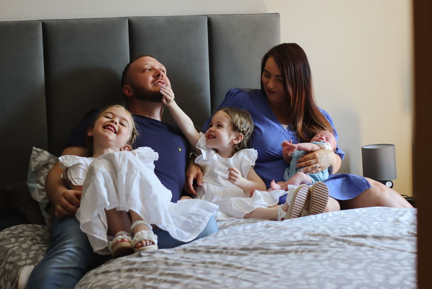 Family relaxing together on a gray upholstered bed with young children.