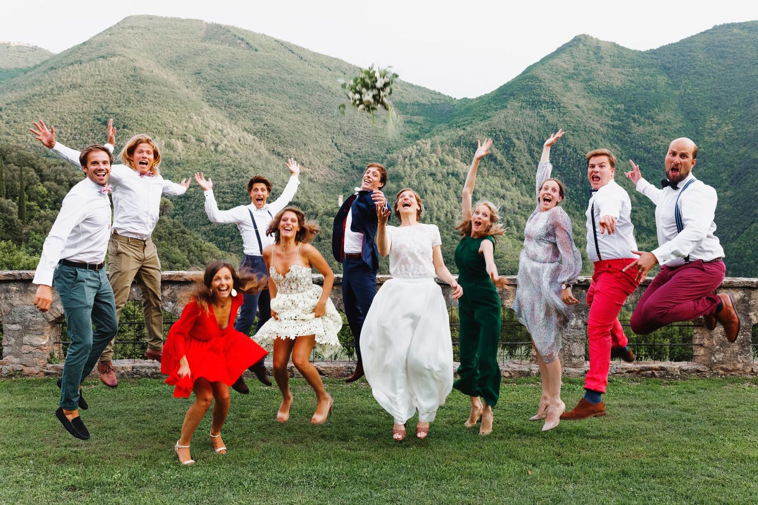 Wedding party joyfully jumps in unison against a backdrop of mountain scenery.