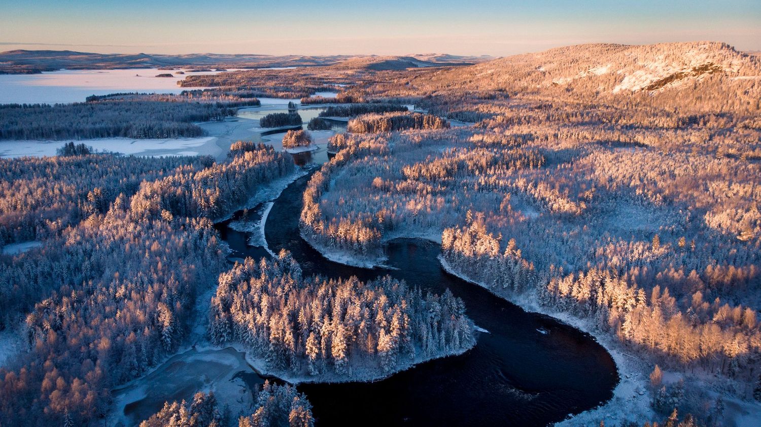 Aerial winter landscape with a winding river through frost-covered forests and snow-dusted hills at golden hour.