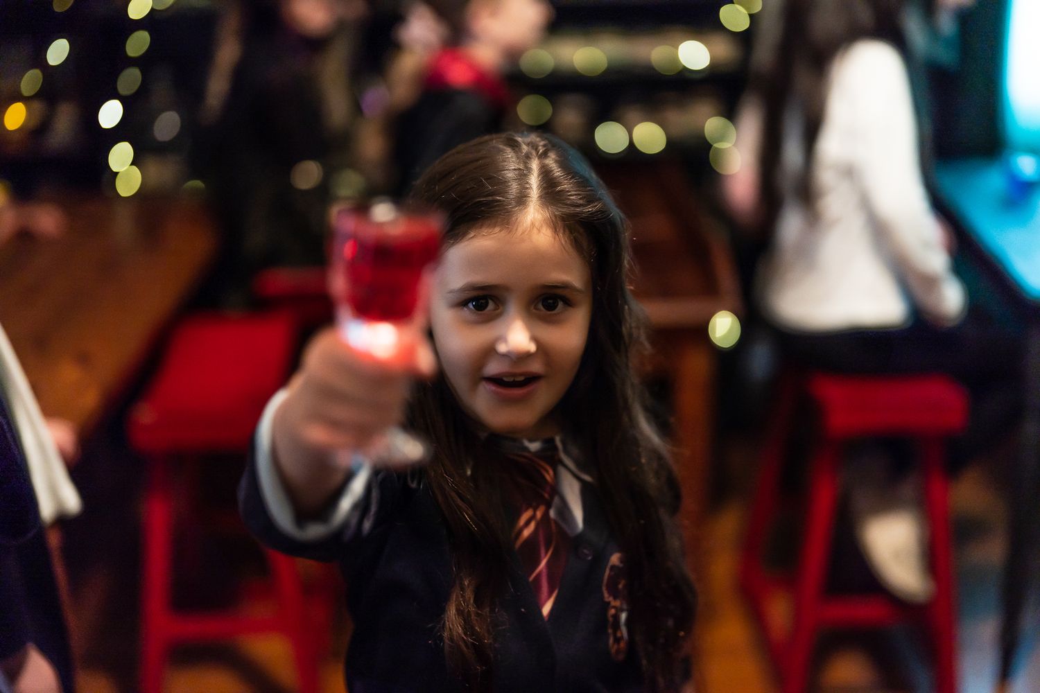 Young girl in school uniform raising a red drink glass at a festive party event.