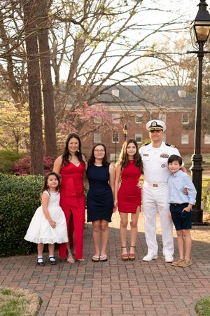 Extended family portrait on brick pathway with military member in dress whites.