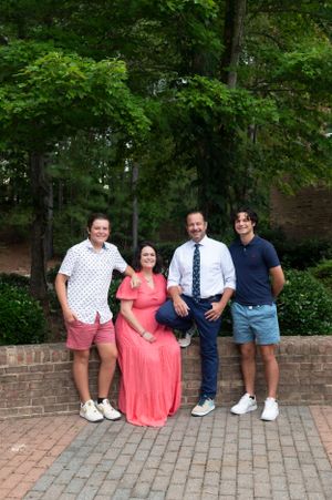 Group sitting casually on brick wall in garden setting wearing coordinated summer outfits.