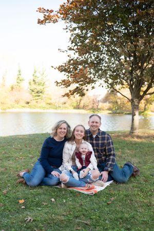 Family lounging on grass during autumn photo session with fall foliage in background.