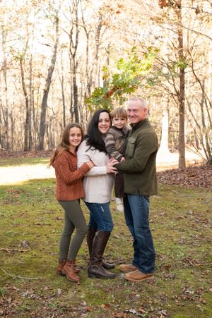 Family playfully posing together on fallen leaves in wooded autumn setting.