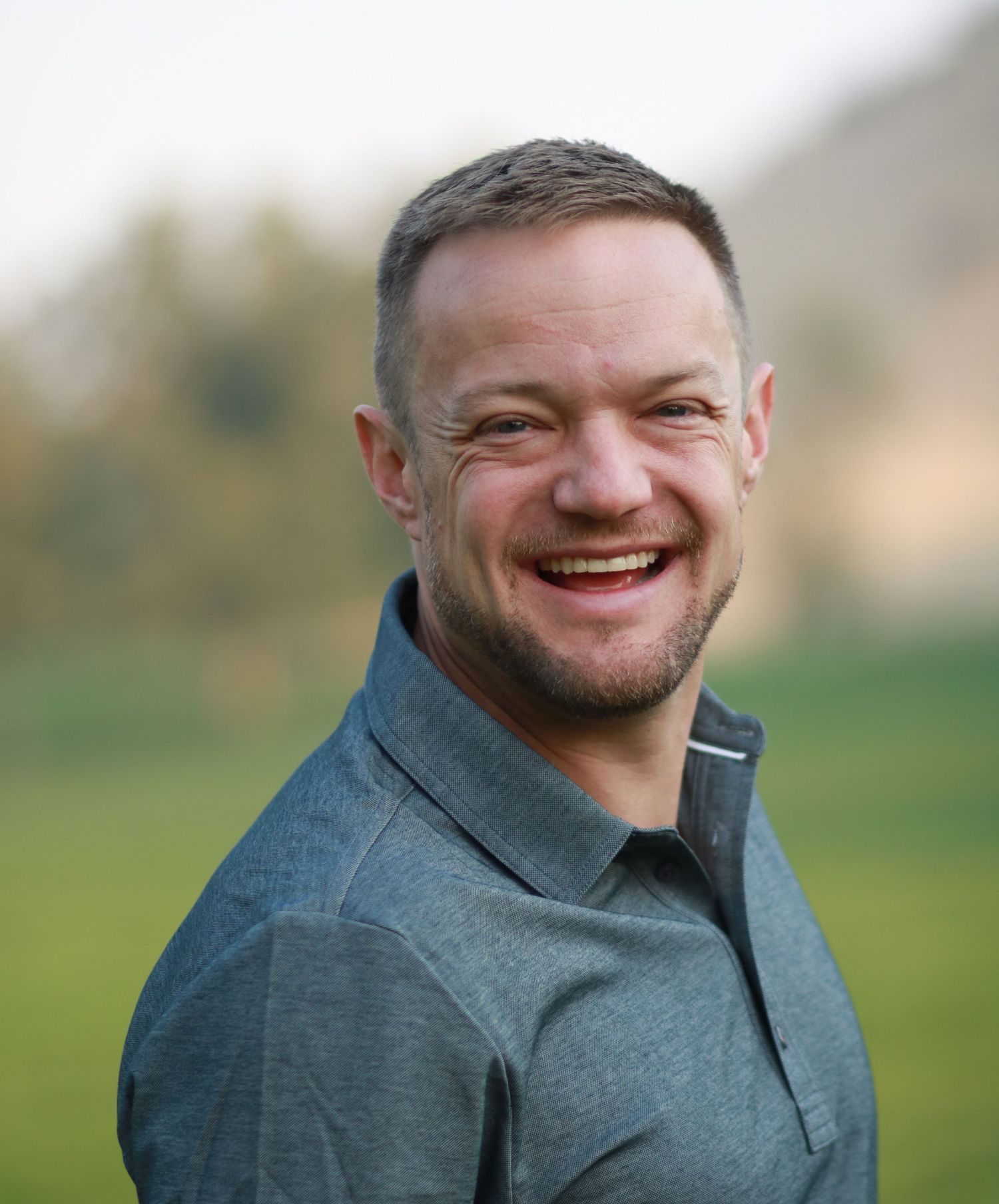 A man in a grey collared polo smiles for professional outdoor headshot