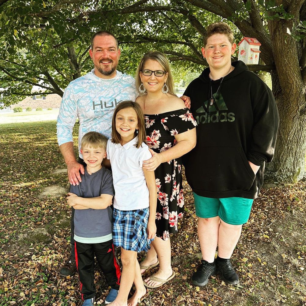 Happy family of five smiling together under a large oak tree on a sunny day outdoors.