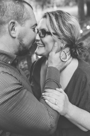 Black and white close-up of a laughing couple sharing an intimate moment, woman wearing glasses and large earrings.