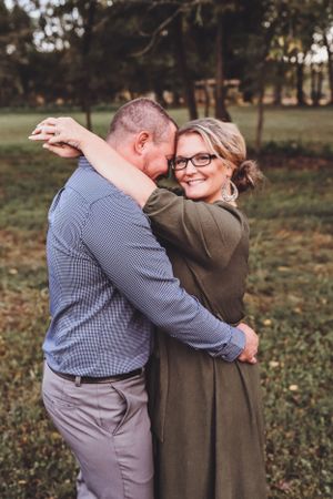 Joyful couple embracing and laughing together while standing on a lush green lawn surrounded by trees.