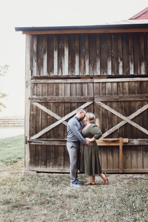 Romantic couple sharing a kiss in front of a rustic wooden barn door on a farm property.
