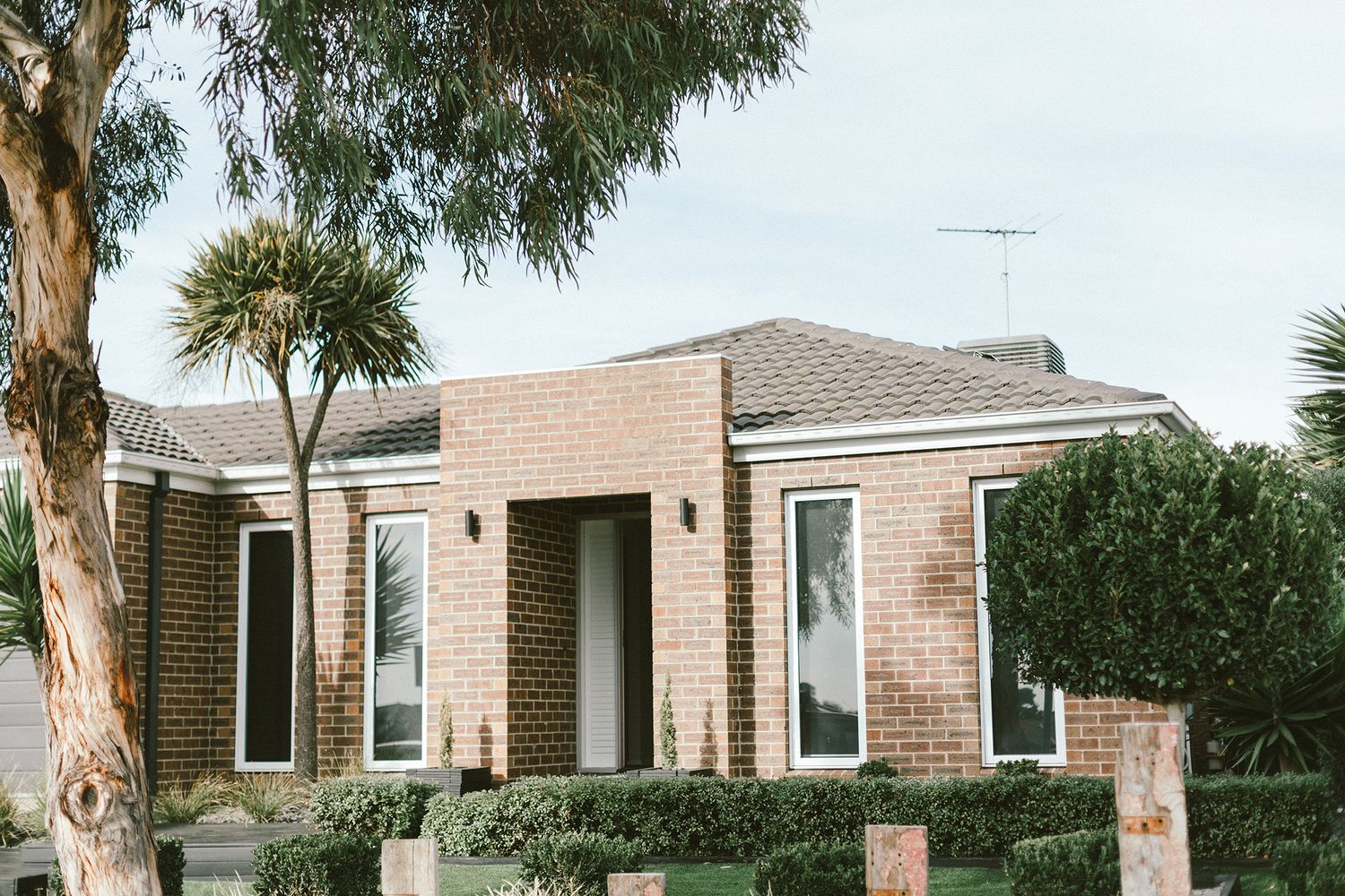 Modern brick house exterior with black shutters and tropical landscaping.