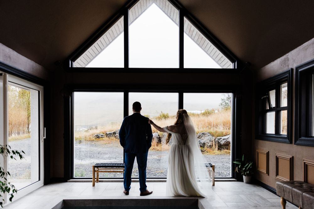 Wedding couple standing by large window in modern cabin with mountain view.