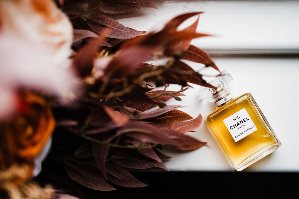 A bottle of Chanel perfume positioned beside burgundy fall flowers.