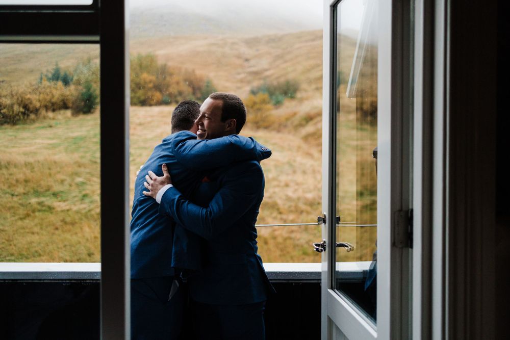 Two people embrace near open window with misty mountain backdrop.